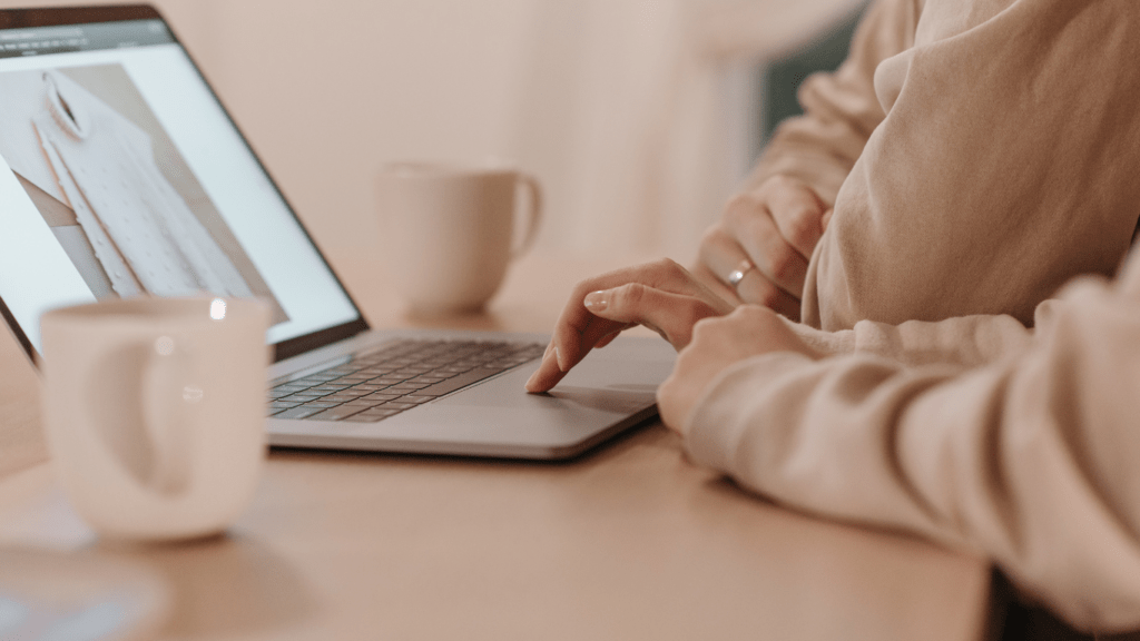 A person typing on a laptop at a desk with a cup of coffee 