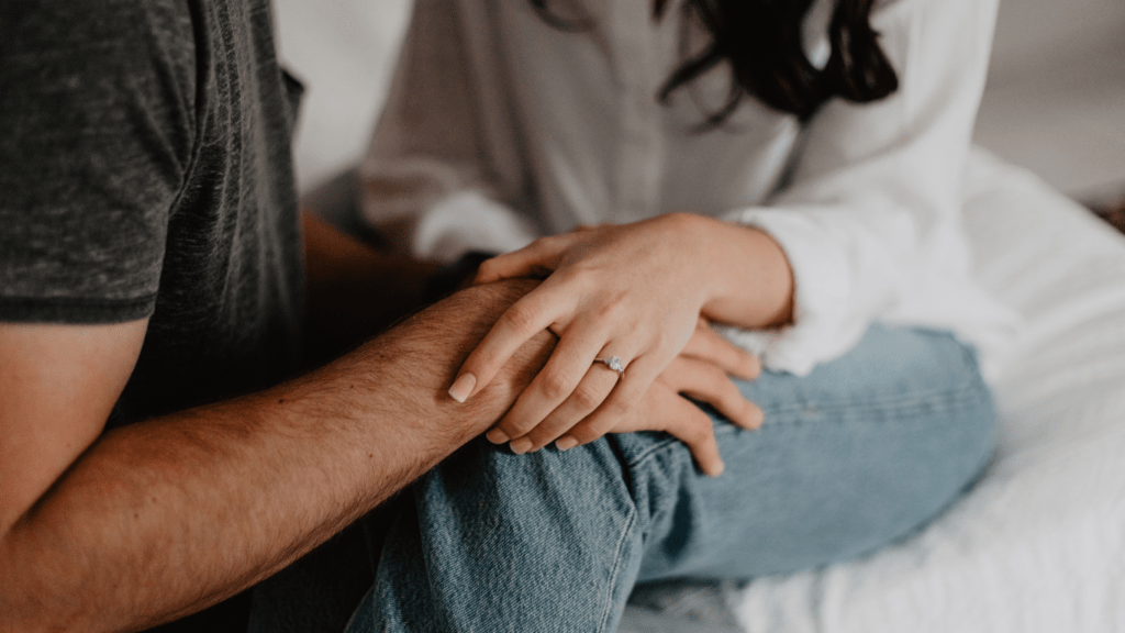 Two people sitting on a bed holding hands