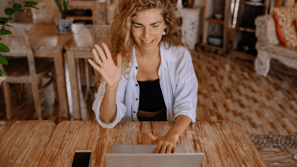 a person sitting at a table with a laptop and waving