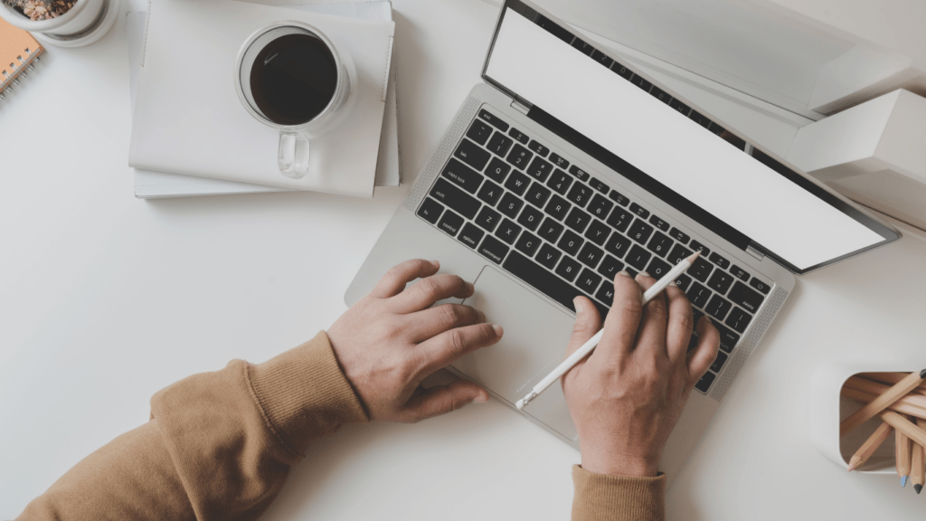 A person typing on a laptop at a desk with a cup of coffee