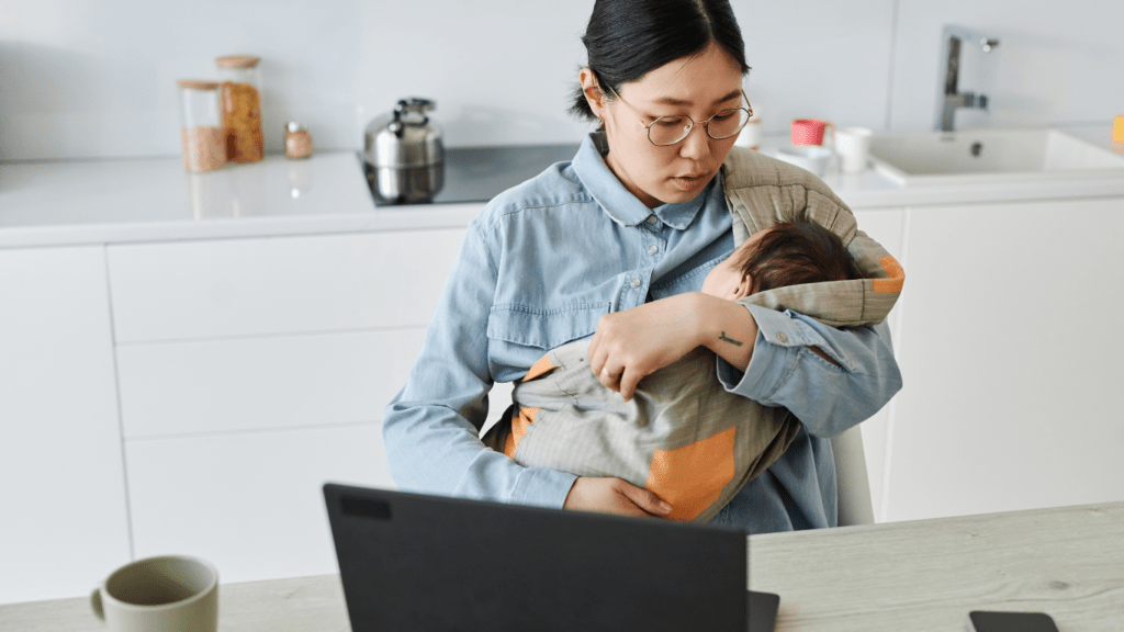 Someone holding a baby while sitting at a desk with a laptop