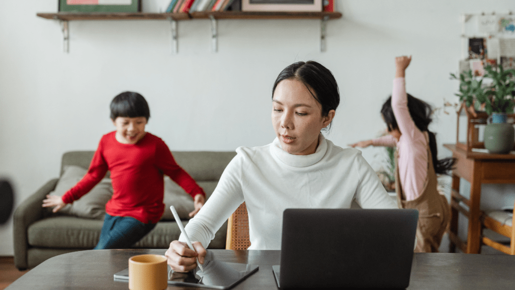 A person working on a laptop in a living room with children in the background