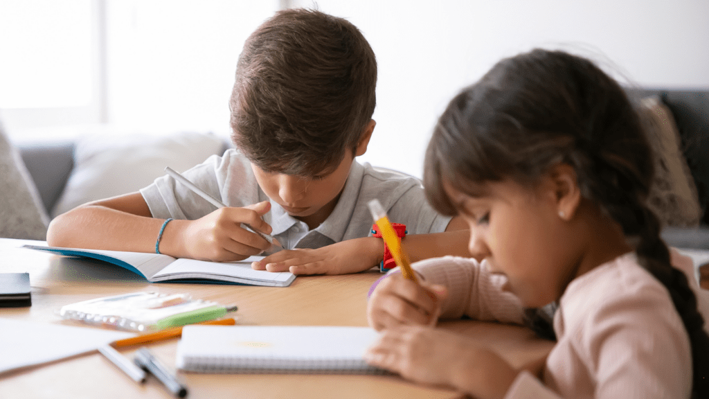 two children sitting at a table with pens and pencils