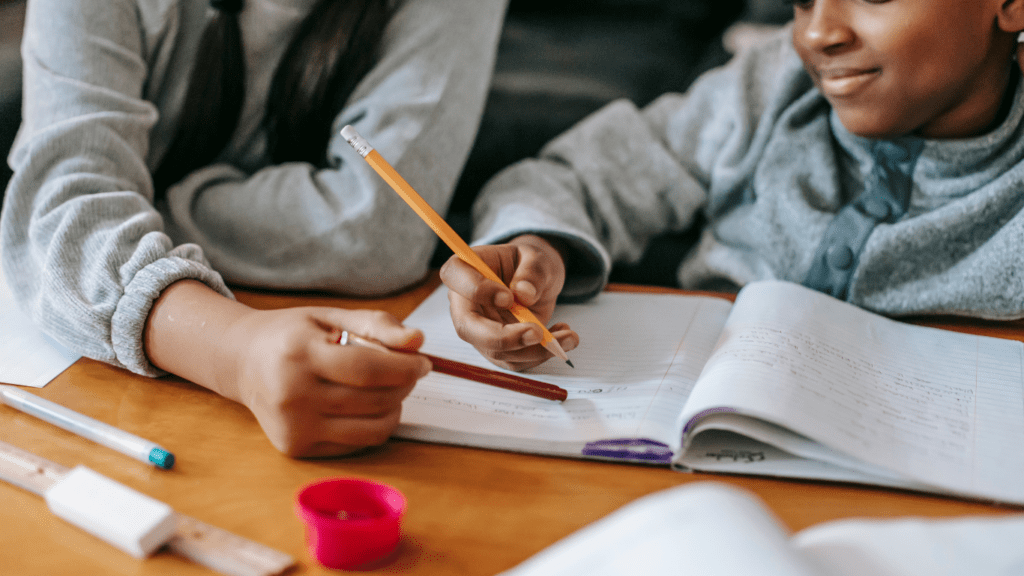 two children sitting at a table with pens and pencils